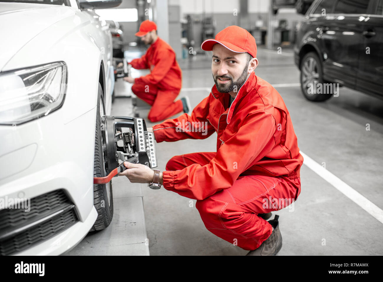 Two auto mechanics in red uniform fixing disk for wheel alignment on a luxury car at the car service Stock Photo