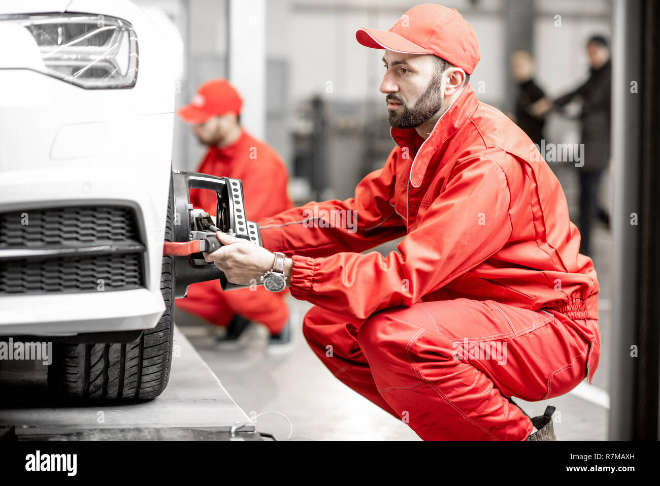 Two auto mechanics in red uniform fixing disk for wheel alignment on a luxury car at the car service Stock Photo