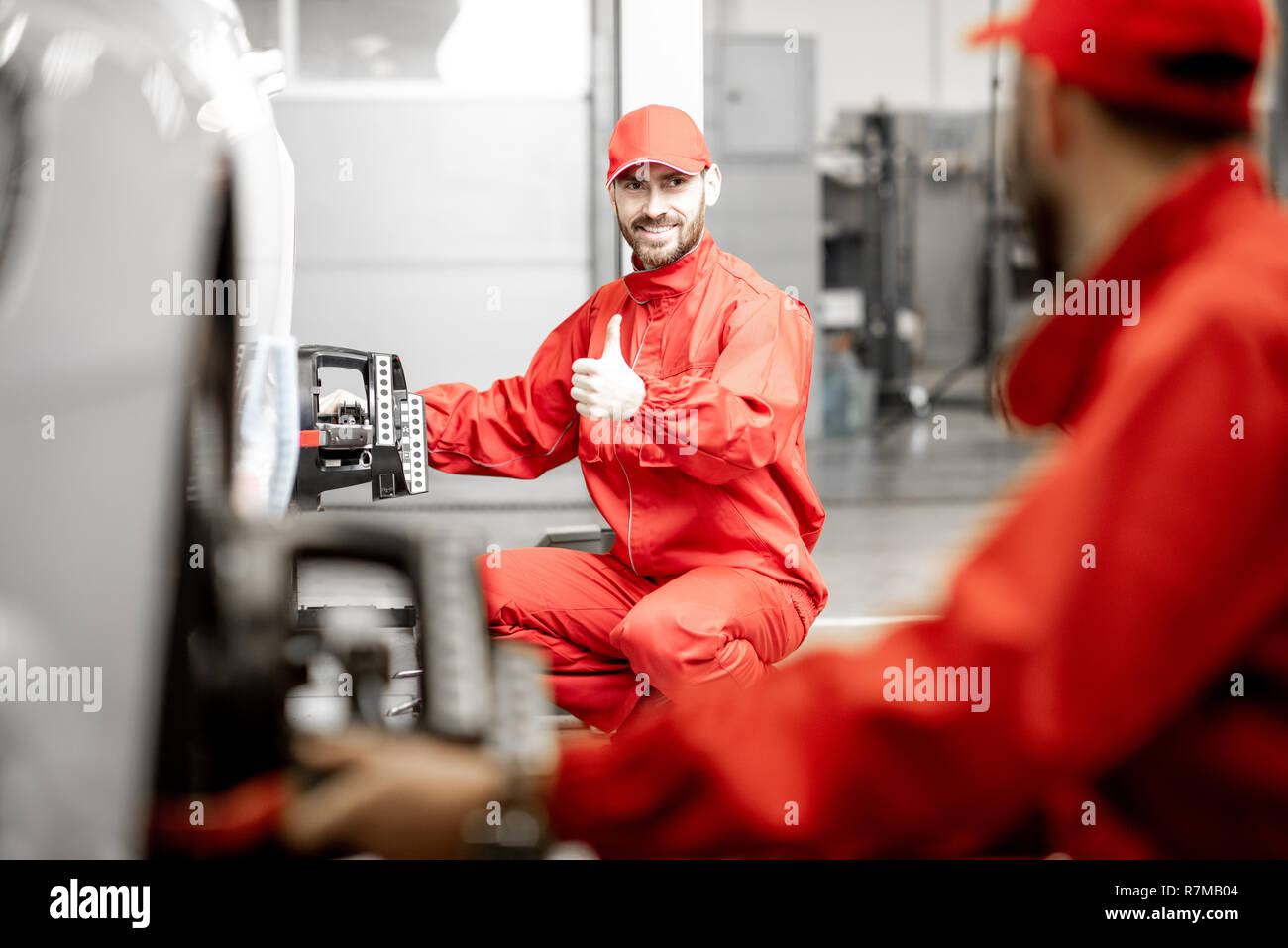 Two auto mechanics in red uniform fixing disk for wheel alignment on a luxury car at the car service Stock Photo