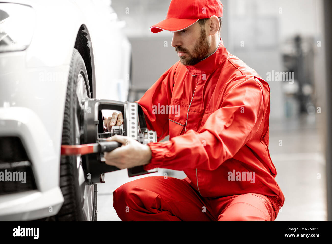 Handsome auto mechanic in red uniform fixing disk for wheel alignment at the car service Stock Photo