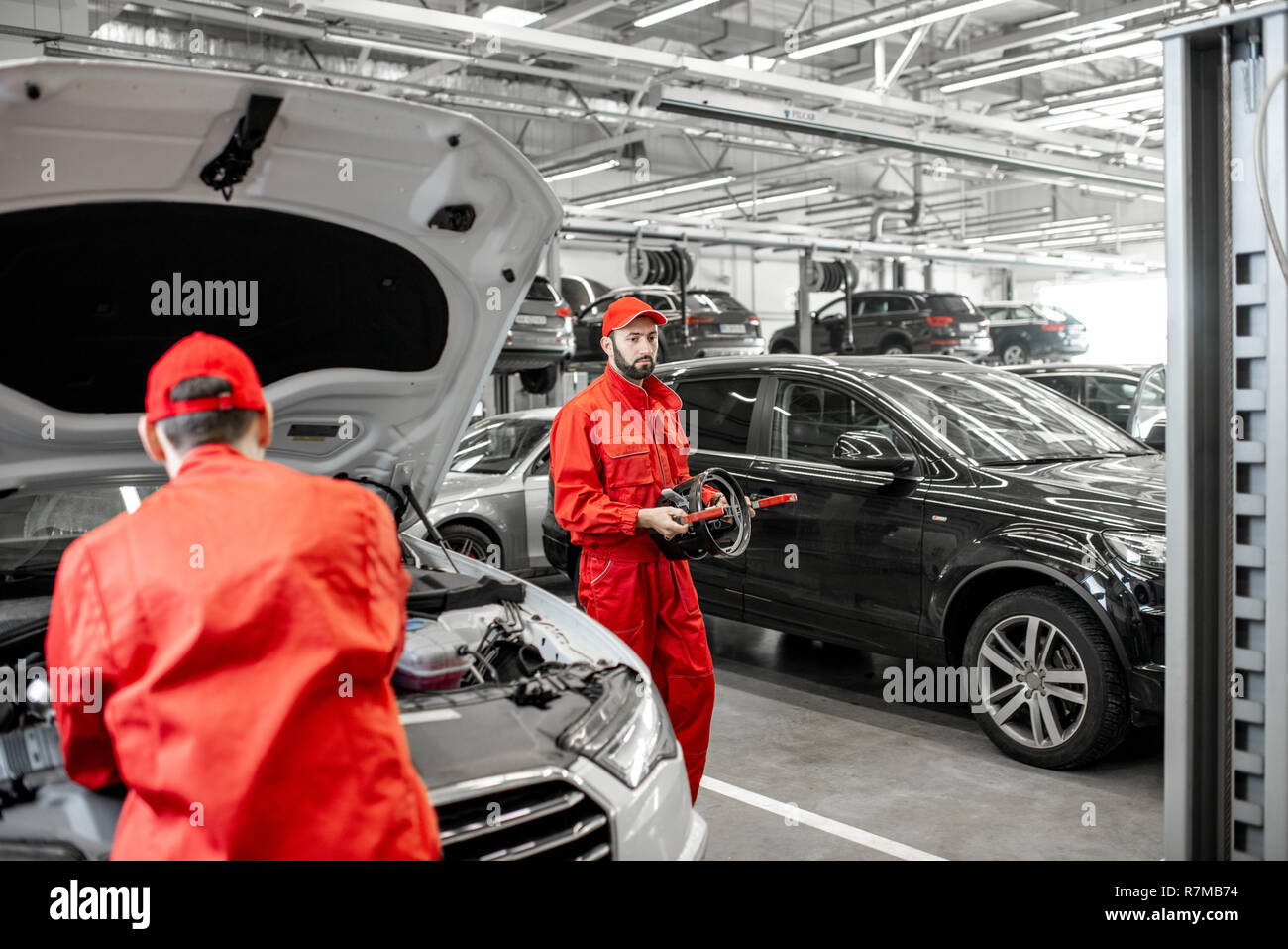 Two handsome auto mechanics in red uniform making wheel alignment with professional tools and computer at the car service Stock Photo