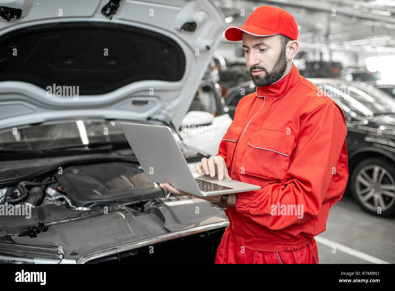 Two auto mechanics in red uniform doing engine diagnostics with computer in the car service Stock Photo
