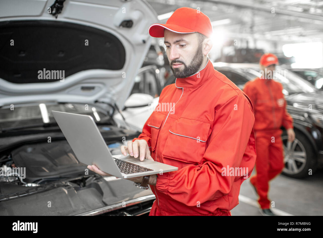Two auto mechanics in red uniform doing engine diagnostics with