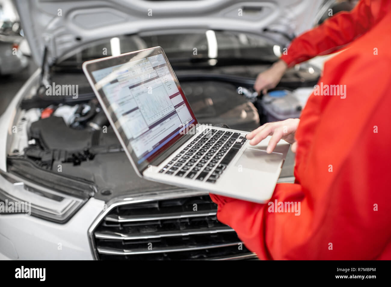 Two auto mechanics in red uniform doing engine diagnostics with