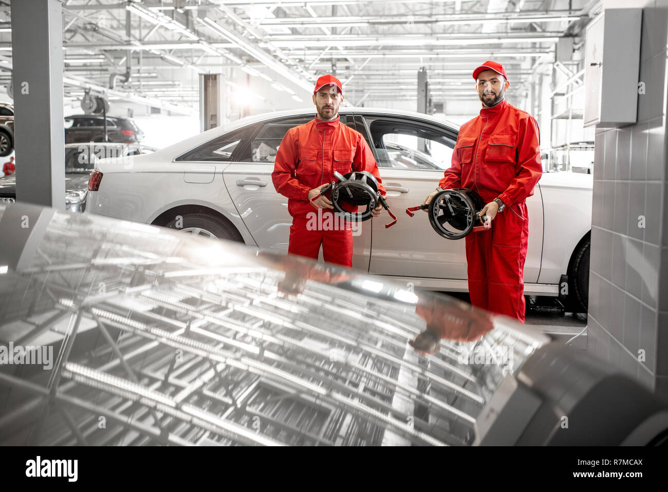 Portrait of two auto mechanics in red uniform standing with disks for wheel alignment at the car service Stock Photo