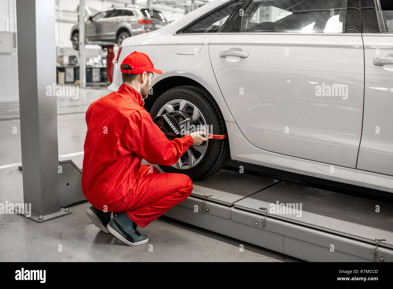 Handsome auto mechanic in red uniform fixing disk for wheel alignment at the car service Stock Photo