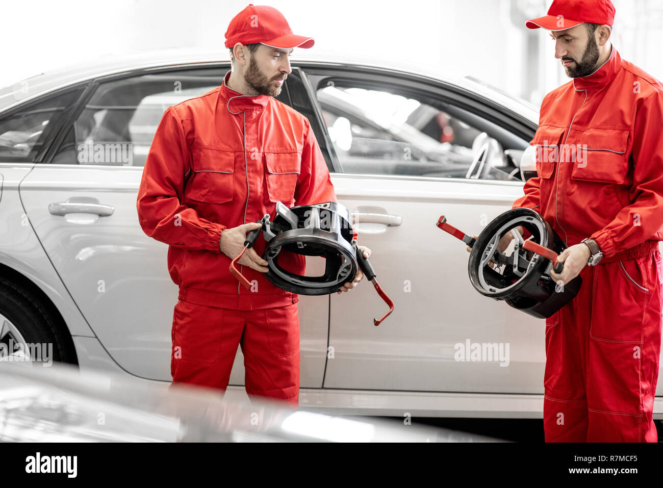 Portrait of two auto mechanics in red uniform standing with disks for wheel alignment at the car service Stock Photo
