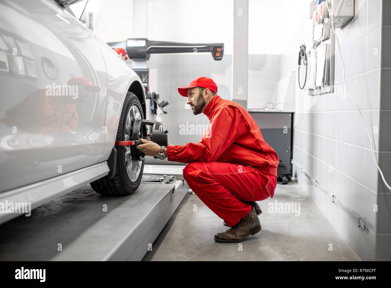 Handsome auto mechanic in red uniform fixing disk for wheel alignment at the car service Stock Photo