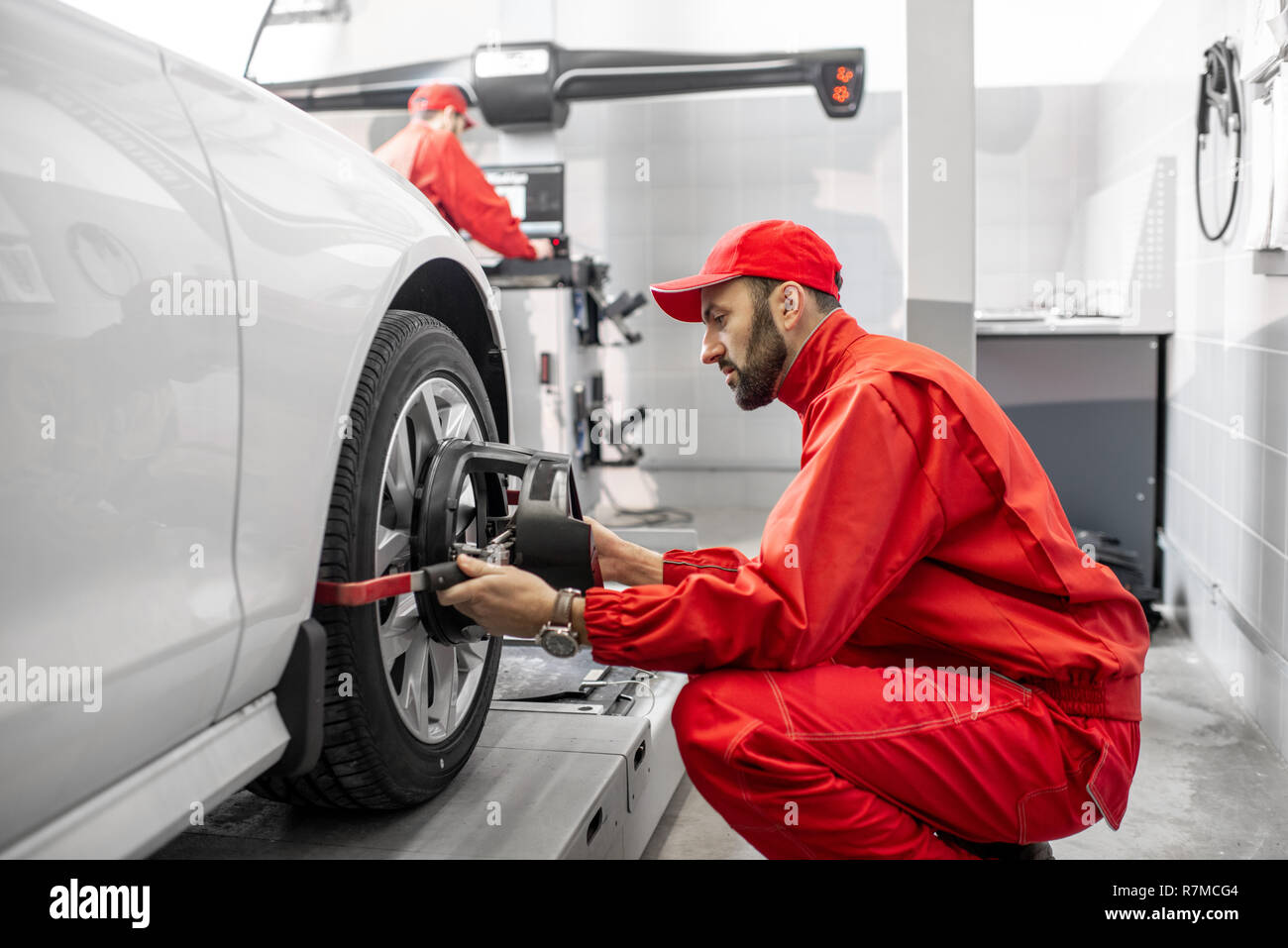Handsome auto mechanic in red uniform fixing disk for wheel alignment