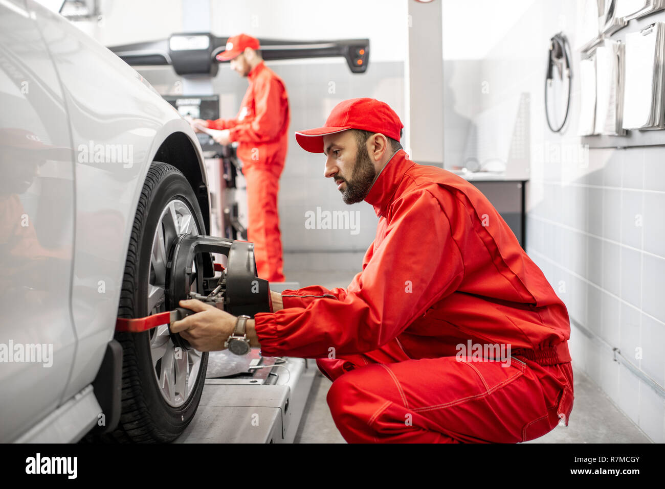 Handsome auto mechanic in red uniform fixing disk for wheel alignment at the car service Stock Photo