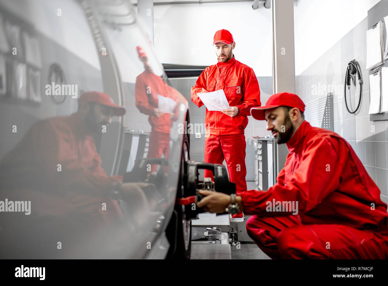 Handsome auto mechanic in red uniform fixing disk for wheel alignment at the car service Stock Photo