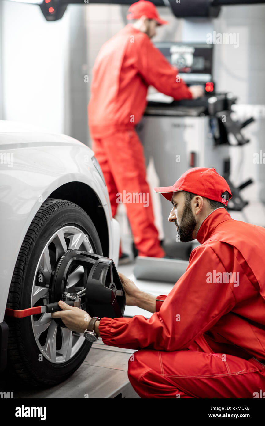 Handsome auto mechanic in red uniform fixing disk for wheel alignment at the car service Stock Photo