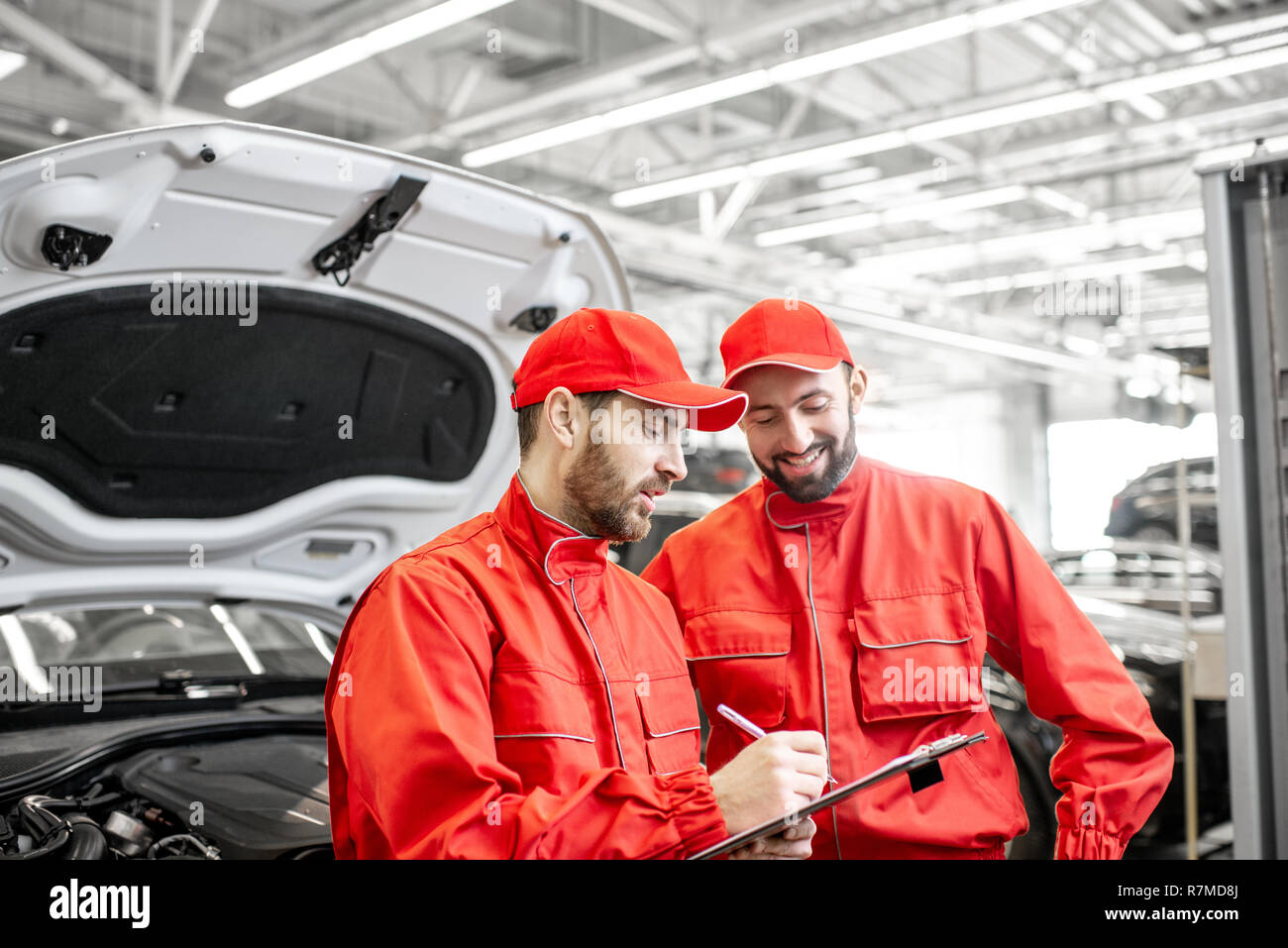Two male auto mechanics in red uniform signing vehicle service documents standing near the car at the car service Stock Photo