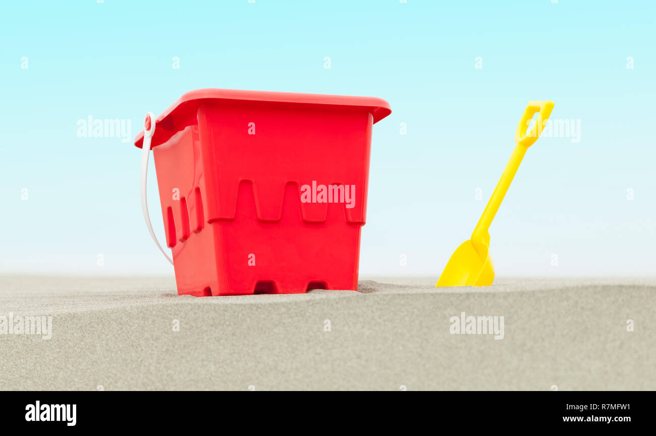 Red Bucket and Yellow Shovel in Beach Sand with Blue Sky. Stock Photo