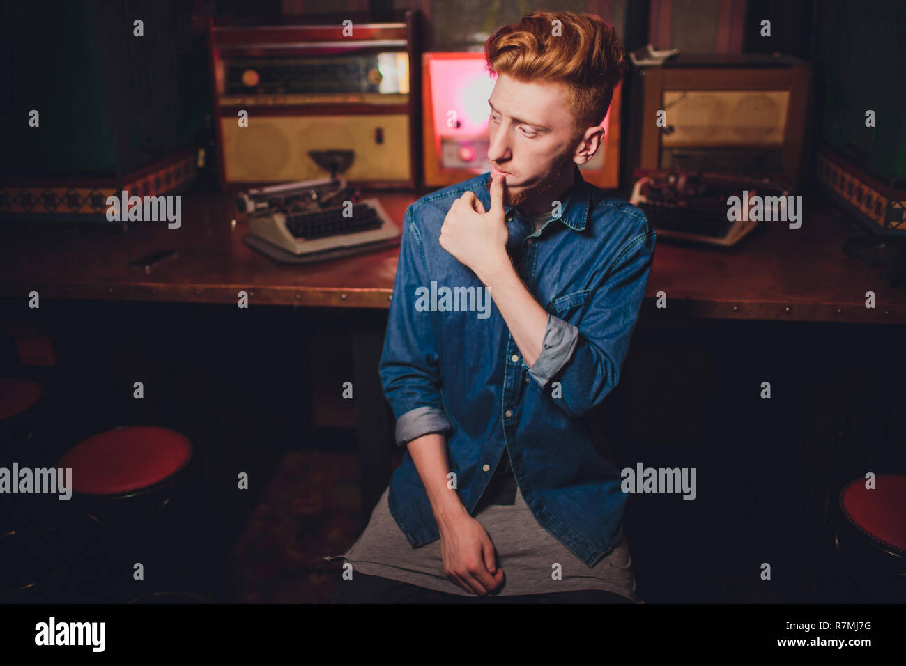 Young man writing on old typewriter. in dark lighting, restaurant, modern clothes, old writer habits Stock Photo