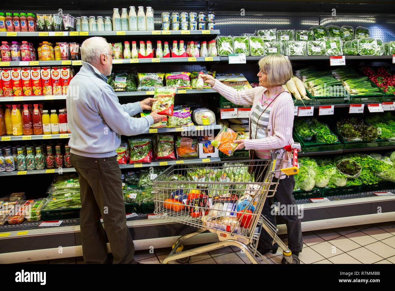 https://c8.alamy.com/comp/R7MMBB/senior-couple-shopping-with-a-shopping-trolley-in-front-of-a-shelf-with-refrigerated-vegetables-in-a-supermarket-germany-R7MMBB.jpg