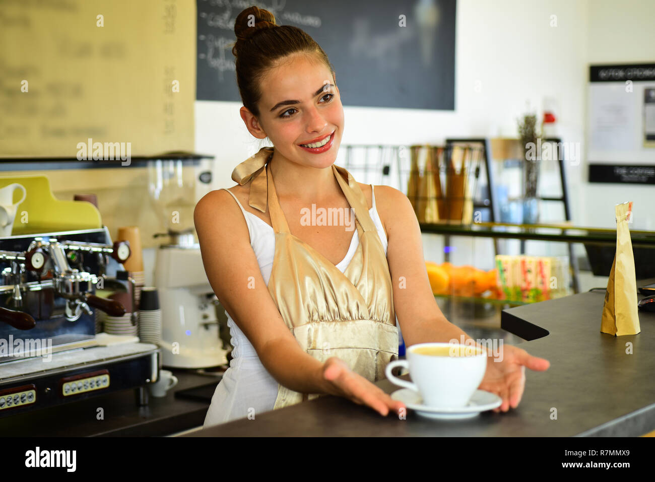 Todays good mood is sponsored by coffee. Woman barista in coffee shop. Barista serve cup of hot coffee drink with smile. Pretty woman stand behind cafe counter. Brewing coffee in coffeehouse Stock Photo