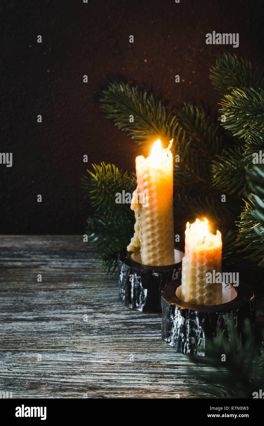 Burning wax candles and fir branches on an old wooden table. Dark