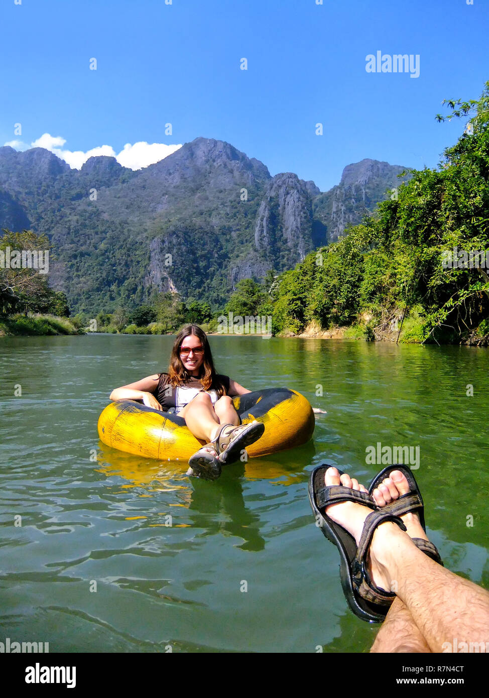 Couple going down Nam Song River in a tube surrounded by karst scenery in Vang Vieng, Laos. Tubing is a popular tourist activity in Vang Vieng. Stock Photo