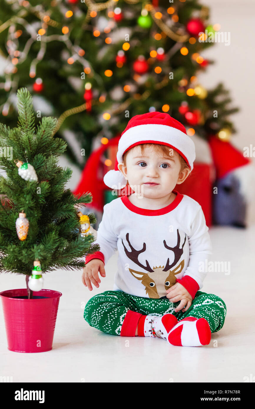 Cute little santa baby in white and green pajamas. Christmas tree