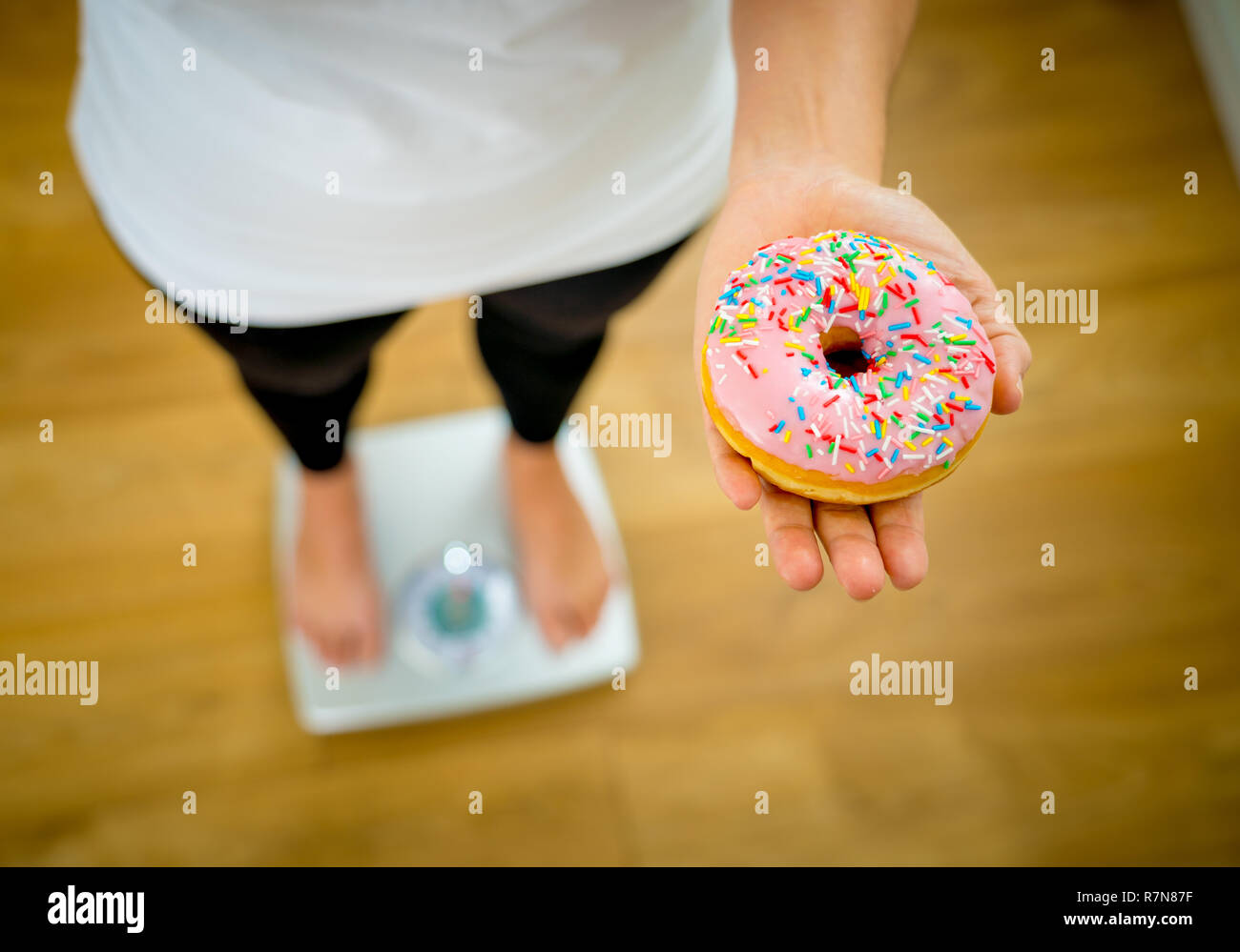 Close up of woman on scale holding on hands apple and doughnut making choice between healthy unhealthy food dessert while measuring body weight in Nut Stock Photo