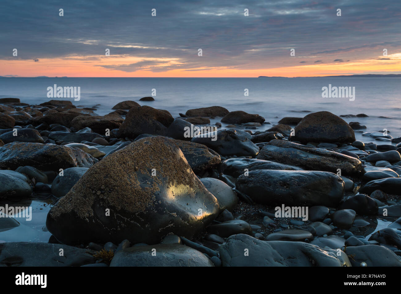 Sunset over the Mull of Galloway from a bouldery beach on the Machars Coast in South-west Scotland. Stock Photo