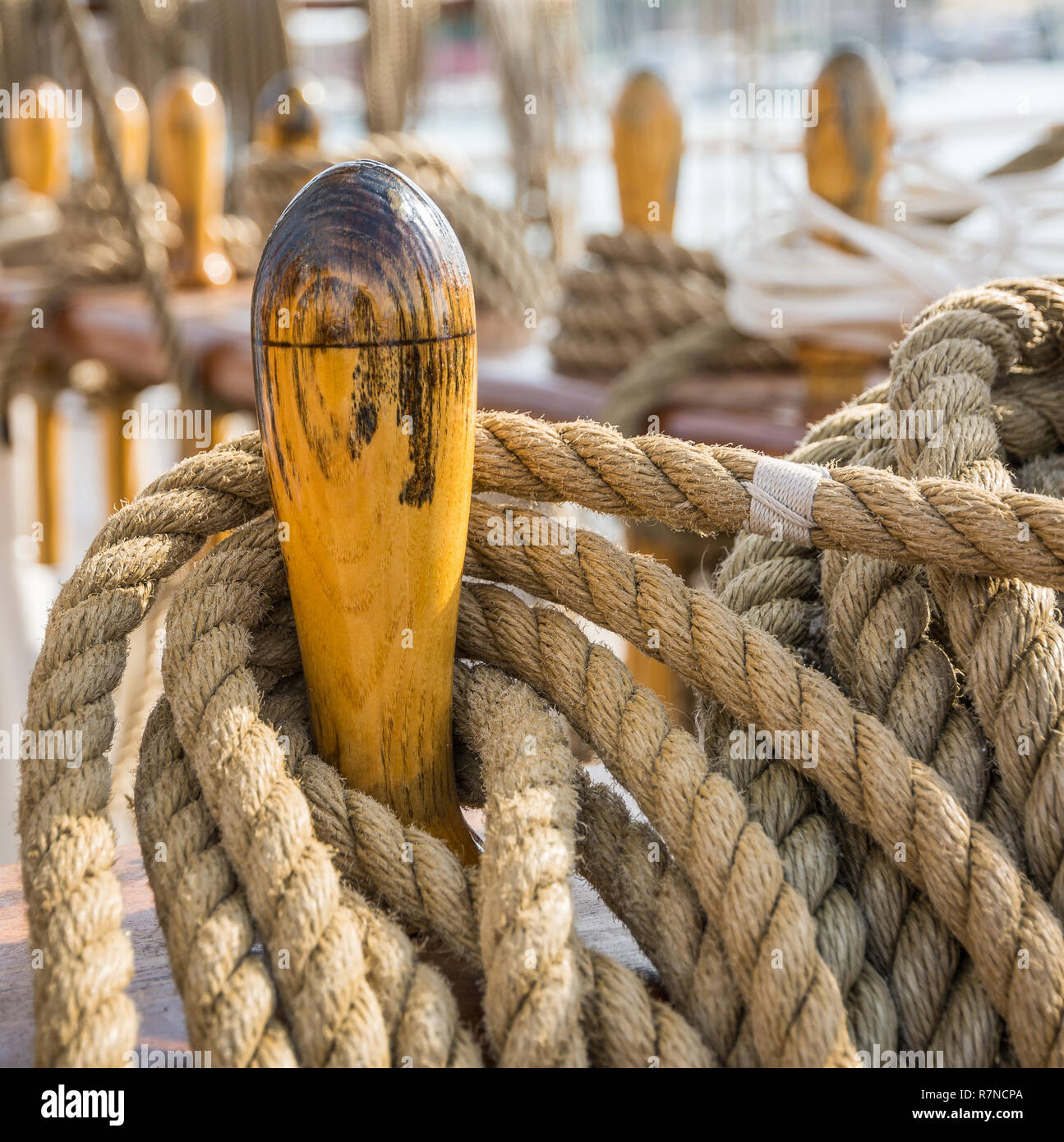 Close-up of bundled ropes on the deck of a sailboat. Detail of wooden cleats with nautical moored ropes. Stock Photo