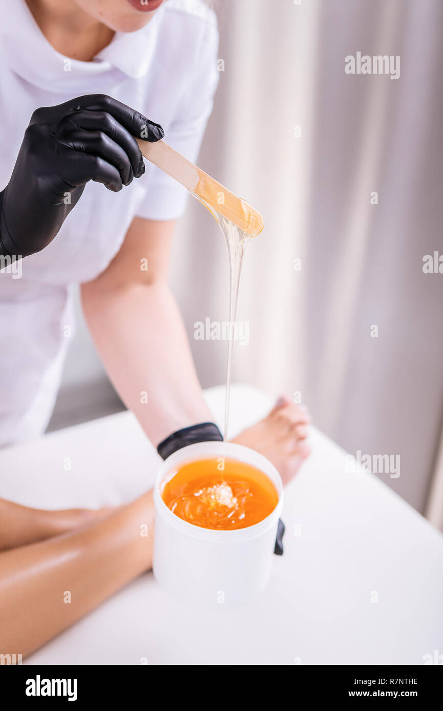 Professional depilation master putting wax on legs of her client Stock Photo