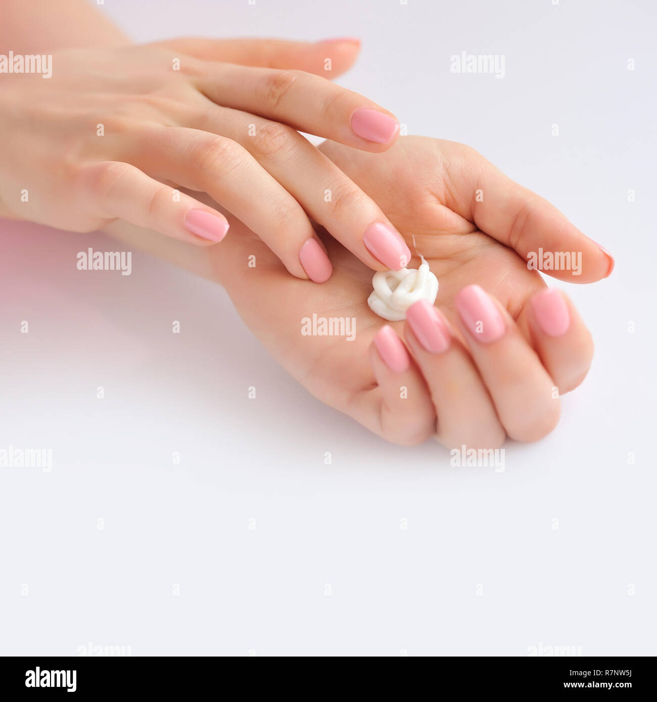 Young woman with pink manicure applies cream on her hands Stock Photo