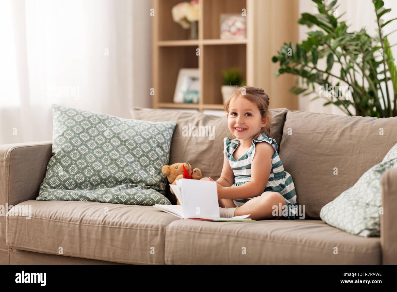 happy girl sitting on sofa with book at home Stock Photo - Alamy