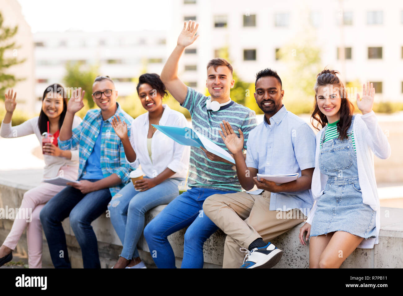 students with notebook waving hands outdoors Stock Photo
