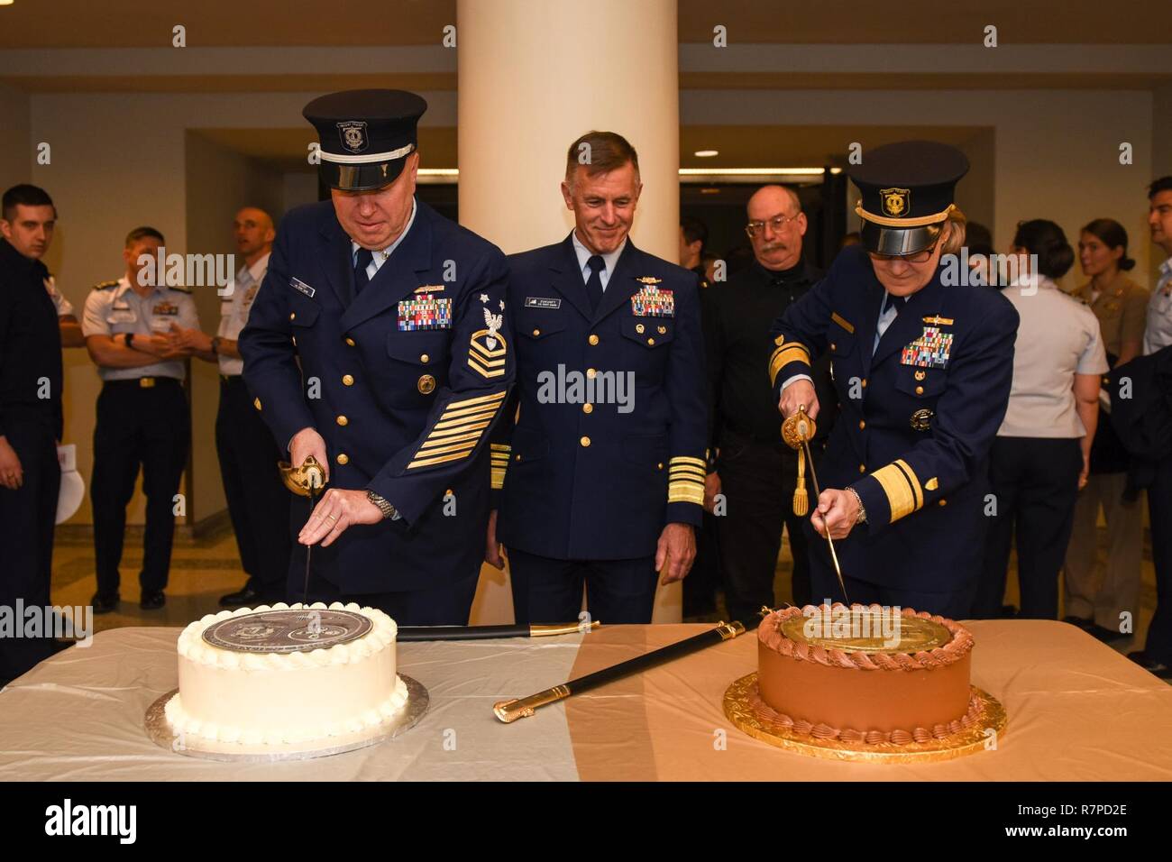 Commandant of the Coast Guard, Admiral Paul Zukunft, watches as the first Ancient Tridents, Rear Admiral Linda Fagan and Master Chief Petty Officer Richard “Shane” Hooker cut their perspective cakes during the Ancient Trident Ceremony held at the Alexander Hamilton Custom House, March 23, 2017. The Ancient Trident Award was established in 2016 to honor the officer and enlisted Coast Guard members with the longest time in the marine safety program. Stock Photo