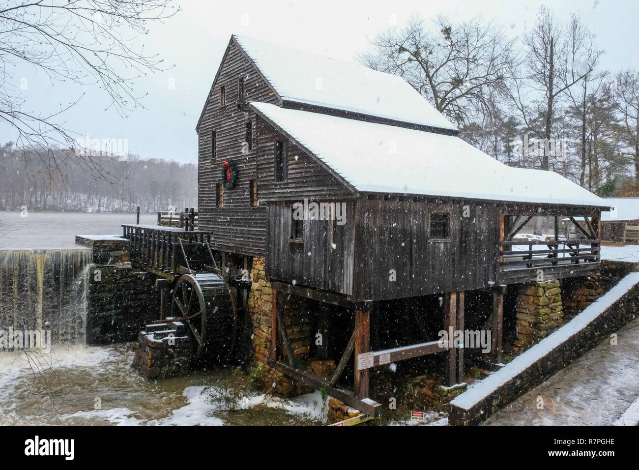 A festive view of the old rustic water mill as snow falls at Historic ...