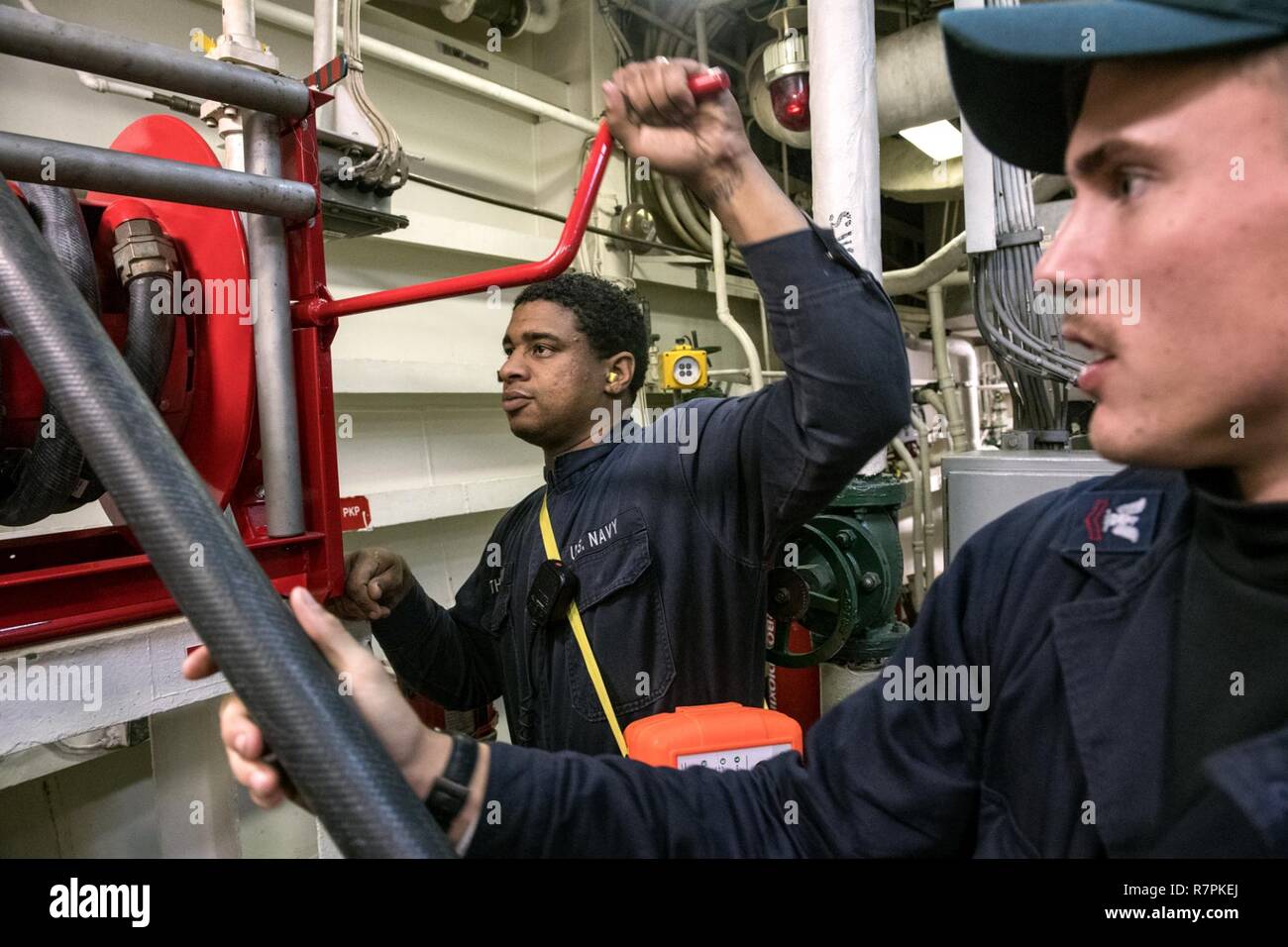 U.S. 7TH FLEET AREA OF OPERATIONS (March 20, 2017) Gas Turbine Systems Technician (Electrical) Fireman Samuel Thompson, from San Diego, left, reels in a fire hose as Machinist’s Mate 2nd Class Dakota Anders, from Hartselle, Alabama, guides it during an engineering training drill aboard Ticonderoga-class guided-missile cruiser USS Lake Champlain (CG 57). Lake Champlain is on a regularly scheduled Western Pacific deployment with the Carl Vinson Carrier Strike Group as part of the U.S. Pacific Fleet-led initiative to extend the command and control functions of the U.S. 3rd Fleet in the Indo-Asia- Stock Photo