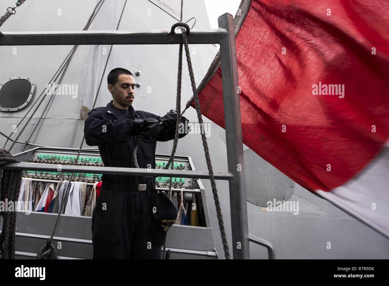 EAST CHINA SEA (March 30, 2017) Quartermaster 3rd Class Anthony Rodriguez, from Hartford, Conn., hoists the hotel flag during a replenishment-at-sea. Green Bay, part of the Bonhomme Richard Expeditionary Strike Group, with embarked 31st Marine Expeditionary Unit, is on a routine patrol, operating in the Indo-Asia-Pacific region to enhance warfighting readiness and posture forward as a ready-response force for any type of contingency. Stock Photo