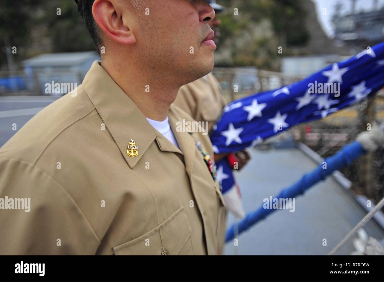 YOKOSUKA, Japan (March 31, 2017) - Senior Chief Hospital Corpsman Michael Jimenez, attached to the U.S. 7th Fleet flagship USS Blue Ridge (LCC 19), performs morning colors in honor of fallen chiefs the day prior to the chief petty officers' 124th birthday. The rank of chief petty officer was officially established on April 1, 1893. Blue Ridge is in an extensive maintenance period in order to modernize the ship to continue to serve as a robust communications platform in the U.S. 7th Fleet area of operations. Stock Photo