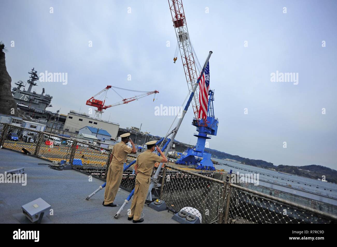YOKOSUKA, Japan (March 31, 2017) - Senior Chief Hospital Corpsman Michael Jimenez, left, and Chief Electrician's Mate Willie Scott II, both attached to the U.S. 7th Fleet flagship USS Blue Ridge (LCC 19), perform morning colors in honor of fallen chiefs the day prior to the chief petty officers' 124th birthday. The rank of chief petty officer was officially established on April 1, 1893. Blue Ridge is in an extensive maintenance period in order to modernize the ship to continue to serve as a robust communications platform in the U.S. 7th Fleet area of operations. Stock Photo