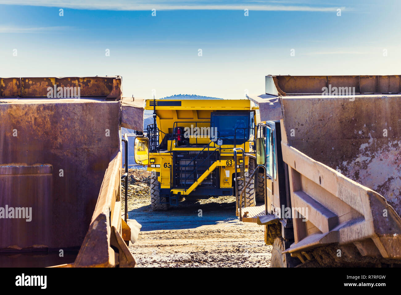 New and heavy quarry truck inside a quarry for mining, between two old quarry trucks in the foreground. Heavy equipment Mining industry. Stock Photo