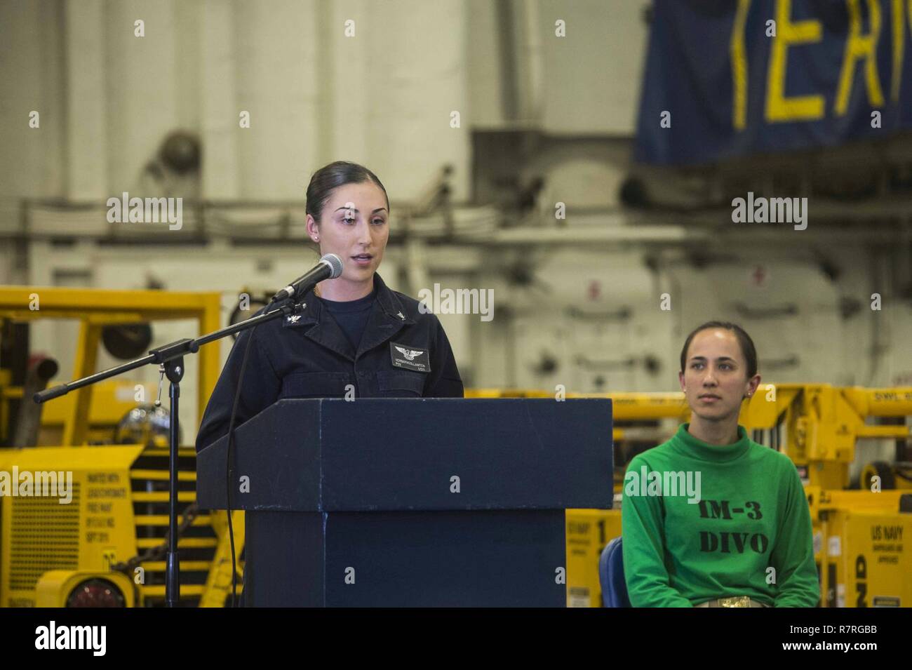 INDIAN OCEAN (March 30, 2017) Aviation Boatswain’s Mate (Handling) 3rd Class Thalia Vergara, from St. Louis, Mo., left, delivers remarks at the women’s history month ceremony in the hangar bay of the amphibious assault ship USS Makin Island (LHD 8), as the event’s emcee, Ensign Kassandra Collins, from West Palm Beach, Fla., listens.  Makin Island, the flagship for the Makin Island Amphibious Ready Group, with the embarked 11th Marine Expeditionary Unit, is operating in the Indo-Asia-Pacific region to enhance amphibious capability with regional partners and to serve as a ready-response force fo Stock Photo
