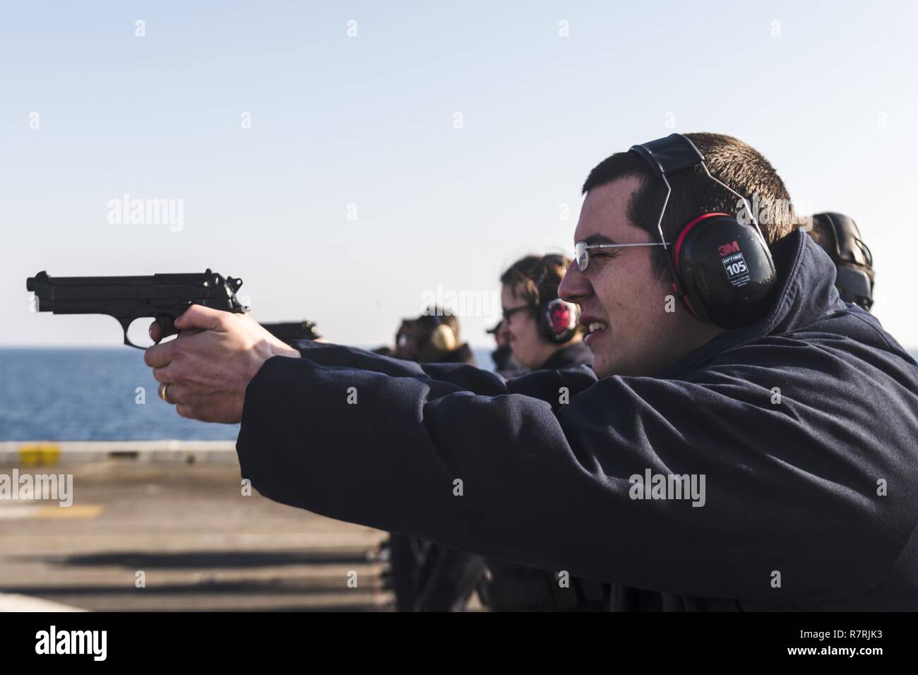 EAST CHINA SEA (April 4, 2017) Information Systems Technician 2nd Class Tyler Newvine, from Flushing, Mich., fires an M9 service pistol during a naval handgun qualification course aboard the amphibious transport dock USS Green Bay (LPD 20). Green Bay, part of the Bonhomme Richard Expeditionary Strike Group, with embarked 31st Marine Expeditionary Unit, is on a routine patrol, operating in the Indo-Asia-Pacific region to enhance warfighting readiness and posture forward as a ready-response force for any type of contingency. Stock Photo