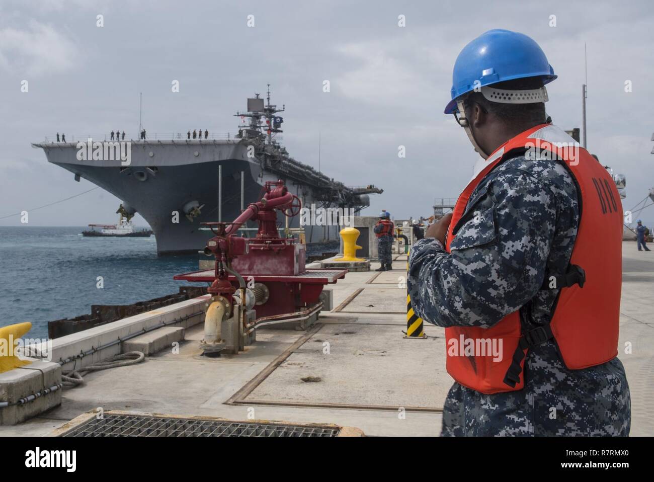 OKINAWA, Japan (April 6, 2017) Machinist’s Mate 3rd Class Gary Benson, from Athens, Ga., assigned to Commander, Fleet Activities Okinawa (CFAO) port operations, performs line handling duties as the amphibious assault ship USS Bonhomme Richard (LHD 6) arrives pierside at White Beach Naval Facility to disembark Marines of the 31st Marine Expeditionary Unit. Bonhomme Richard, flagship of the Bonhomme Richard Amphibious Ready Group, is on a patrol, operating in the Indo-Asia-Pacific region to enhance warfighting readiness and posture forward as a ready-response force for any type of contingency. Stock Photo