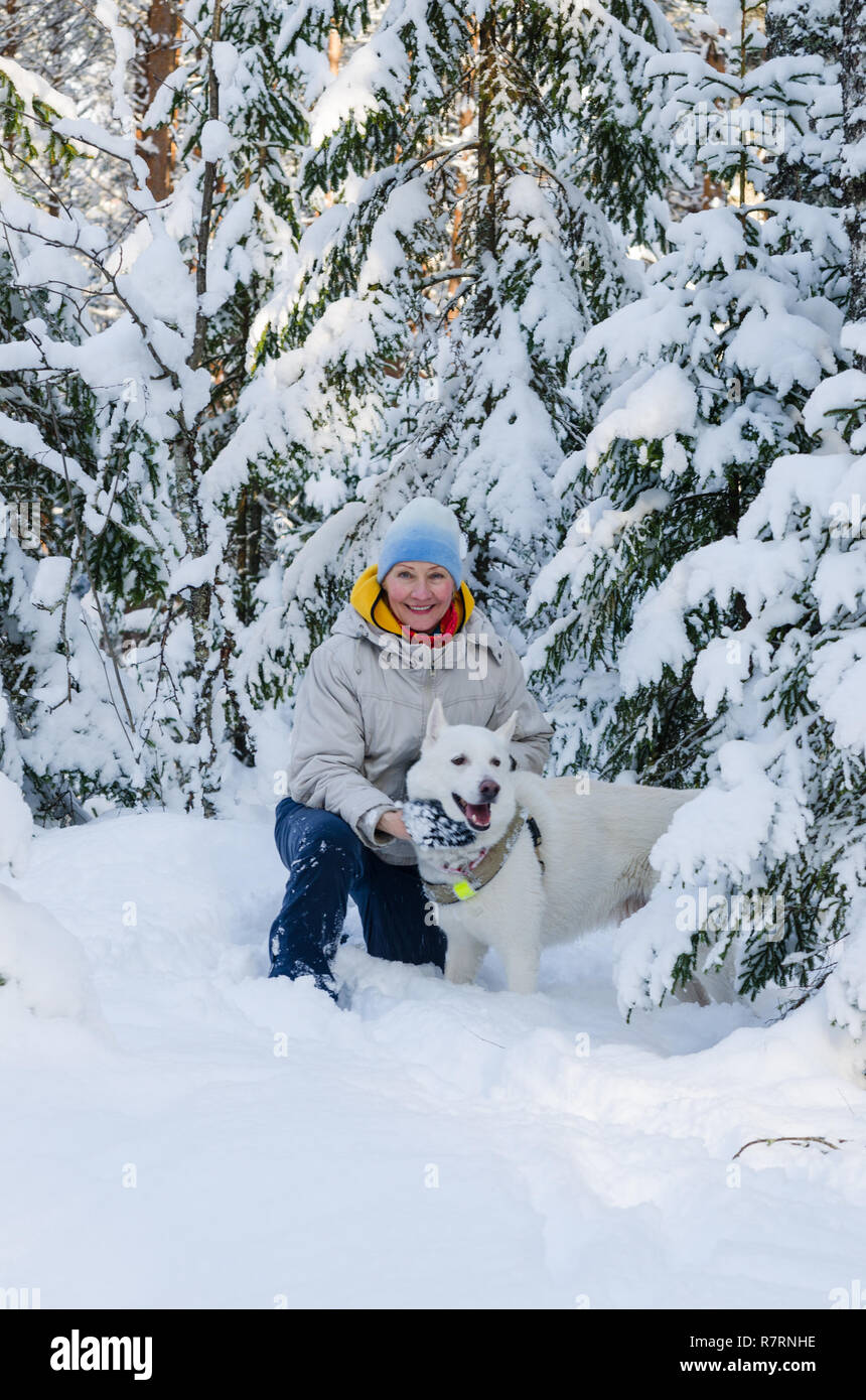 Joyful woman with a white dog in the winter snow-covered forest Stock Photo