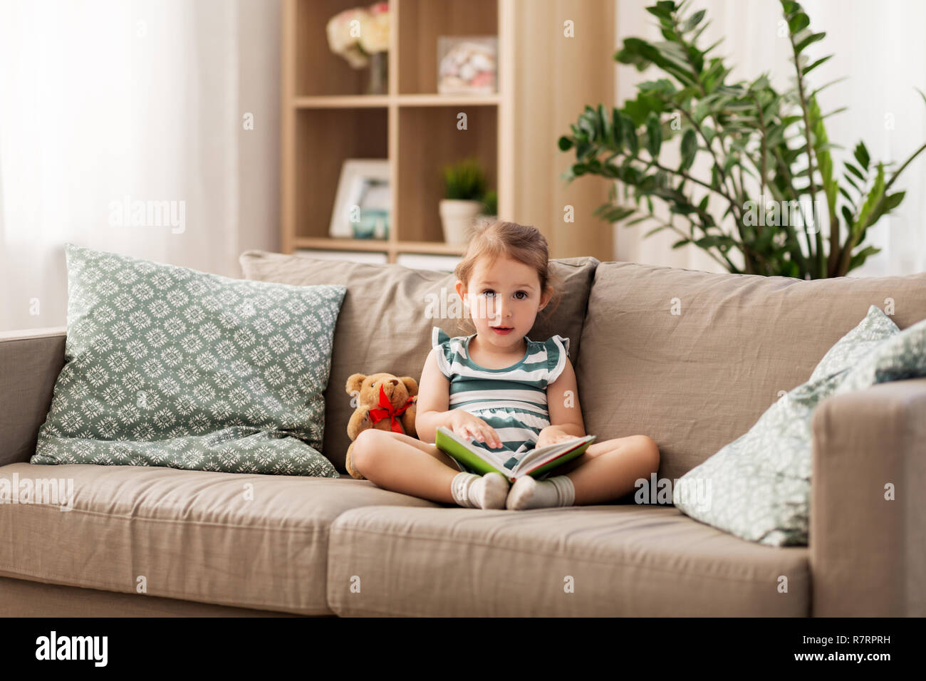 happy girl sitting on sofa with book at home Stock Photo - Alamy