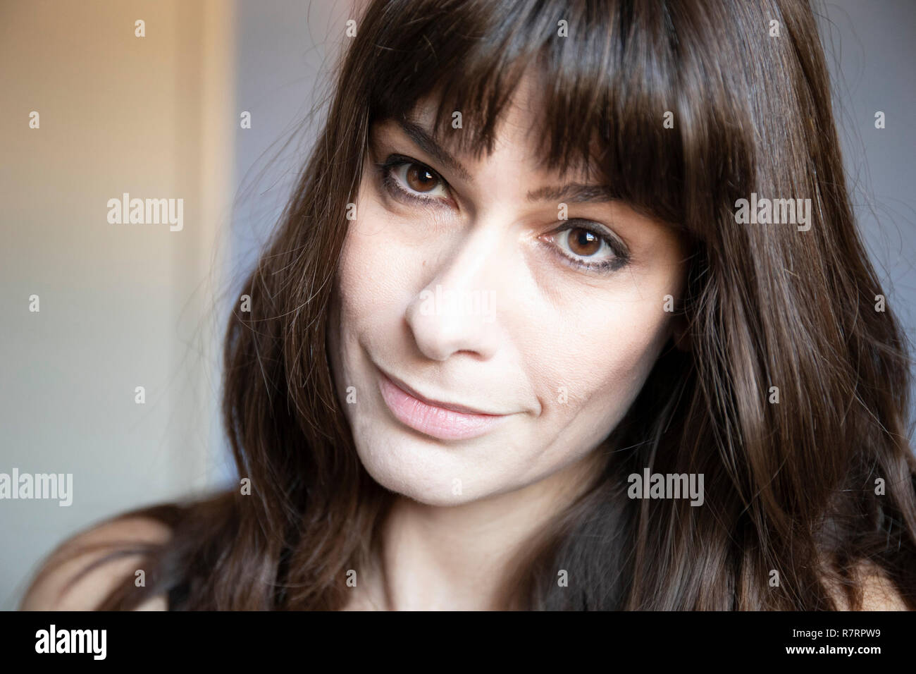 Young woman close-up portrait. Caucasian with brown long hair and bangs. Smiling expression, tilted head. Stock Photo