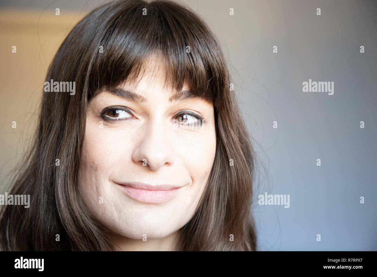 Young woman close-up portrait. Caucasian with brown long hair and bangs. Smiling expression, looking right. Stock Photo