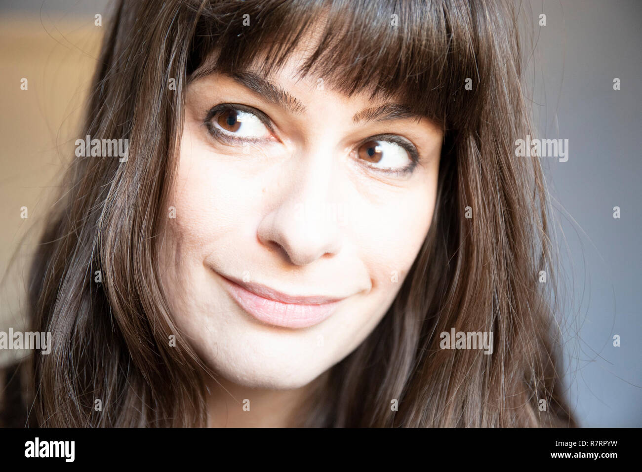 Young woman close-up portrait. Caucasian with brown long hair and bangs. Smiling expression with dimples, looking right. Stock Photo