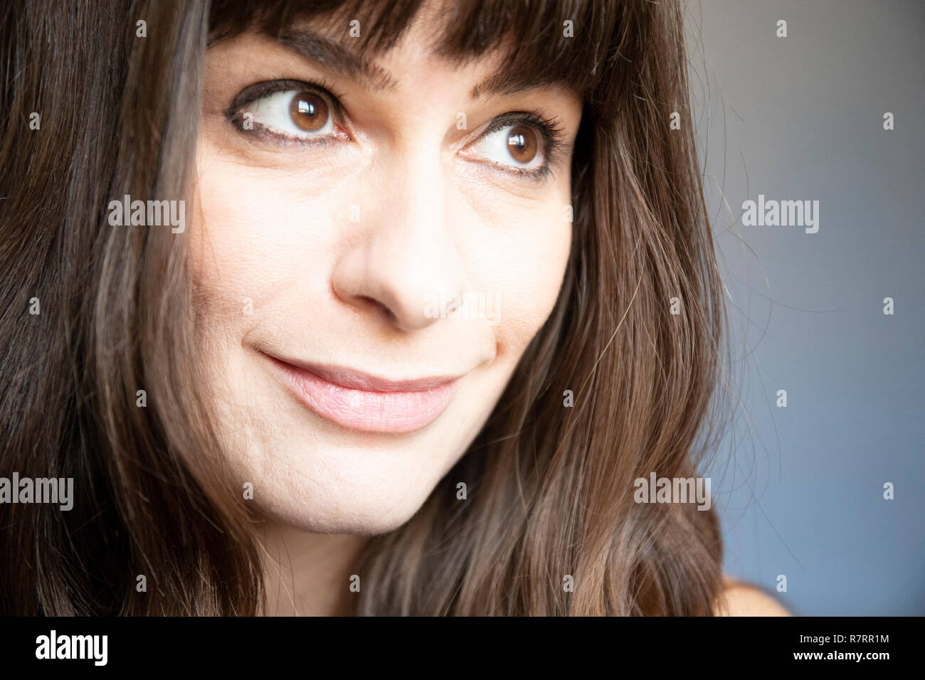 Young woman close-up portrait. Caucasian with brown long hair and bangs. Smiling expression, looking left. Stock Photo