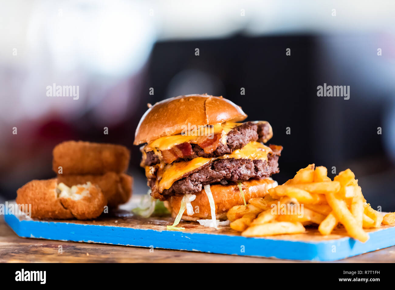 Burger greasy stacked street food, fried french fries closeup, melted cheese and bun on blue