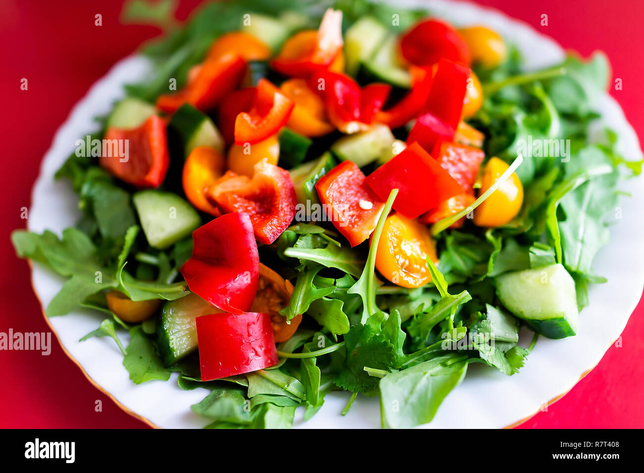 Closeup of fresh raw, chopped vegetable sald with arugula greens, red and orange bell peppers, tomatoes, cucumbers on table, colorful vibrant healthy  Stock Photo