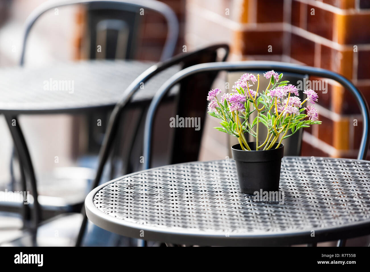Closeup of empty table outside restaurant cafe metal chair on sidewalk street, purple flowers, flowerpot potted setting, nobody Stock Photo